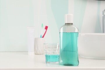 Bottle of mouthwash, toothbrushes and glass on white table in bathroom