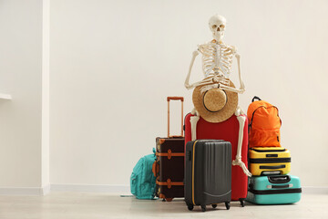 Waiting concept. Human skeleton with hat and suitcases indoors, space for text