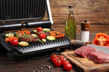 Electric grill with meat, spices and vegetables on wooden table