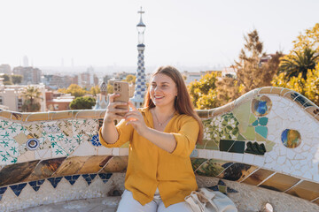Beautiful female in Gaudi garden, Spain, Barcelona. Young traveling woman taking selfie outdoors. Concept of travel, tourism and vacation in city