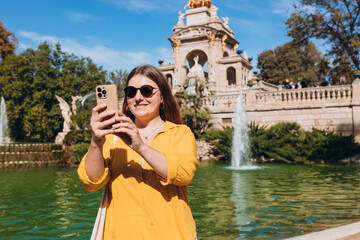 Young female tourist visiting Ciutadella Park in Barcelona. Young traveling woman taking selfie outdoors. Concept of travel, tourism and vacation in city. Use technology concept, Traveling Europe