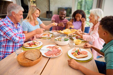 Three Generation Family Indoors Around Table At Home Serving And Eating Meal Together