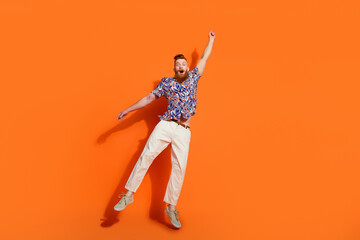 Full size photo of astonished man with red beard wear stylish shirt fly catching object in empty space isolated on orange color background