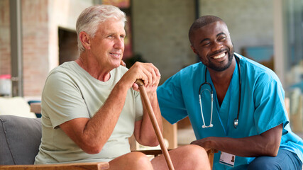 Male Nurse Visiting Senior Man Using Walking Stick With Mobility Issues At Home