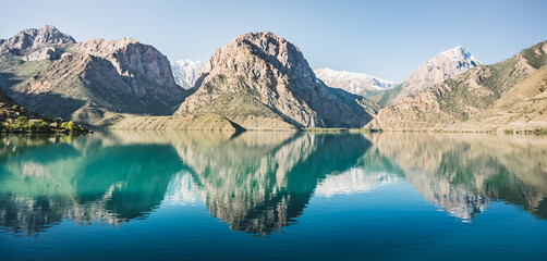 Panoramic view of blue Iskanderkul lake and rocky mountains in Tajikistan, the mountain range is reflected in the water of the lake in the early morning