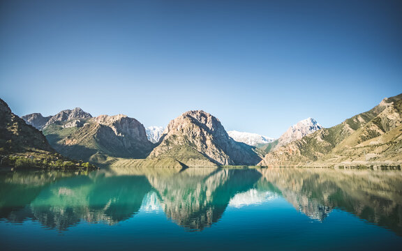 Panoramic view of blue Iskanderkul lake and rocky mountains in Tajikistan, the mountain range is reflected in the water of the lake in the early morning