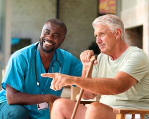 Male Nurse Visiting Senior Man Using Walking Stick With Mobility Issues At Home