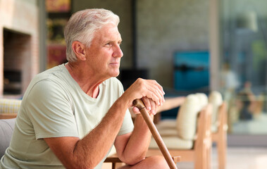 Independent Senior Man Holding Walking Stick Sitting In Chair At Home 