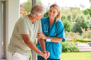 Female Nurse Visiting Senior Man Using Walking Stick With Mobility Issues At Home