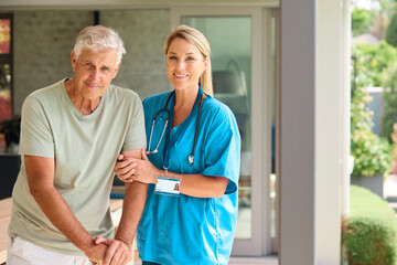 Portrait Of Female Nurse Visiting Senior Man Using Walking Stick With Mobility Issues At Home