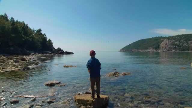 A boy throwing stones into the water on the beach. Montenegro.