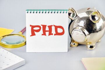 Doctorate of Philosophy concept. PhD on a vertically standing notebook near a piggy bank, a magnifying glass and a calculator
