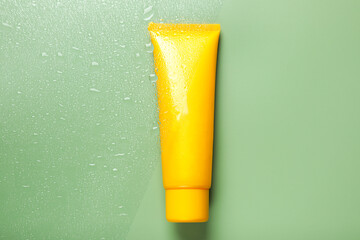 Tube with moisturizing cream on wet green surface, top view