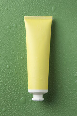 Moisturizing cream in tube on green background with water drops, top view