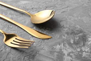 Stylish golden cutlery set on grey textured table, closeup. Space for text