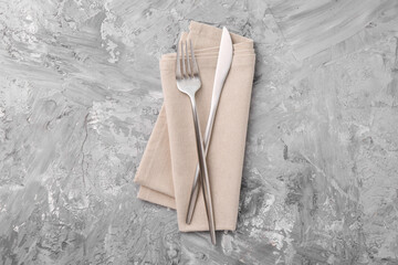Elegant silver cutlery and kitchen towel on grey textured table, top view