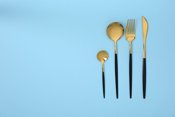 Stylish golden cutlery set on light blue background, flat lay. Space for text