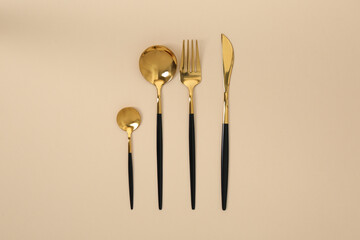 Stylish golden cutlery set on beige background, flat lay