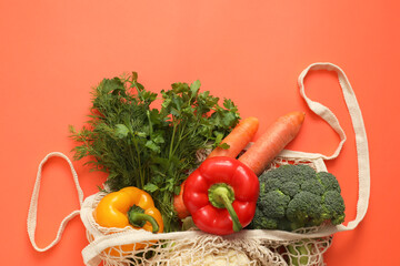 String bag with fresh vegetables and herbs on coral background, top view. Space for text