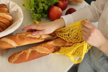 Woman taking baguettes out from string bag at countertop, closeup