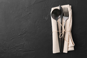 Set of stylish cutlery and napkin on black table, top view. Space for text