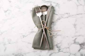 Set of stylish cutlery and napkin on white marble table, top view
