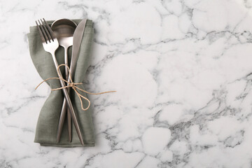 Set of stylish cutlery and napkin on white marble table, top view. Space for text