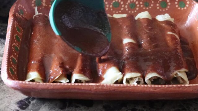 Slow motion still shot of spoon pouring mole sauce on tacos enchiladas. enmoladas mexican food