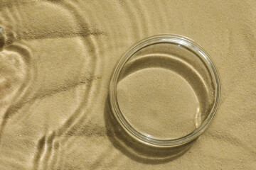 Stylish presentation for product. Glass podium in water on sand, top view. Space for text