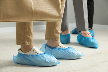Women wearing blue shoe covers onto different footwear indoors, selective focus
