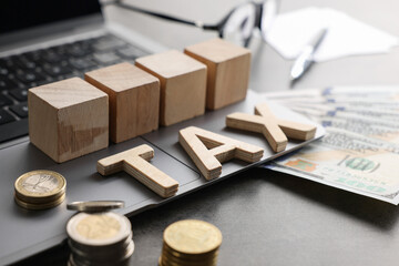 Word Tax made of wooden letters, cubes, laptop, banknotes and coins on grey table