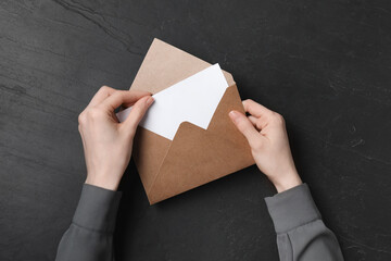 Woman taking card out of letter envelope at black textured table, top view
