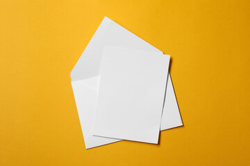 Blank sheet of paper and letter envelope on orange background, top view