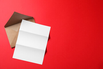 Blank sheet of paper and letter envelope on red background, top view. Space for text
