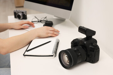 Photographer working on computer at white table with camera indoors, closeup