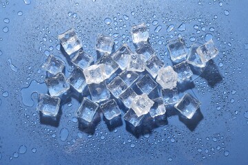 Melting ice cubes and water drops on blue background, flat lay