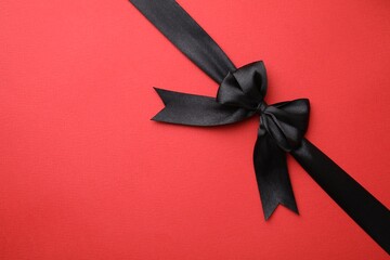 Black satin ribbon with bow on red background, top view. Space for text
