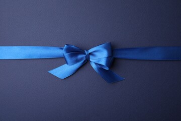 Bright satin ribbon with bow on blue background, top view