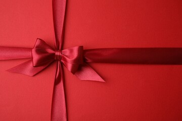 Bright satin ribbon with bow on red background, top view