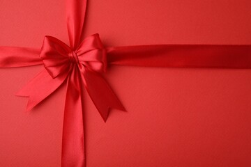 Bright satin ribbon with bow on red background, top view