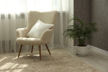 Soft white pillow on armchair and houseplant near window indoors