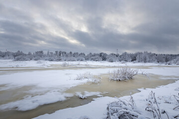 Rural winter landscape with a river, forest with a church and a cell phone tower on the horizon.