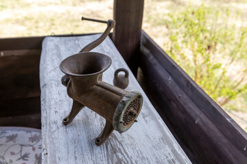 An antique cast iron meat grinder sits on a rustic wooden table, showing signs of age and use with its rust and patina.
