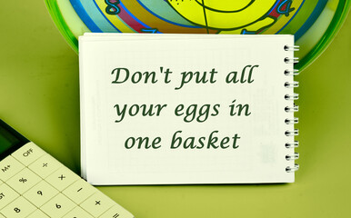Don't put all your eggs in one basket Message on a notepad on the background of a clock next to a calculator