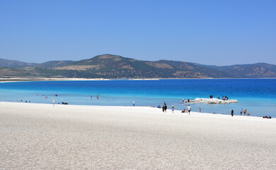 a beach with white sand, blue water and a mountain in the background