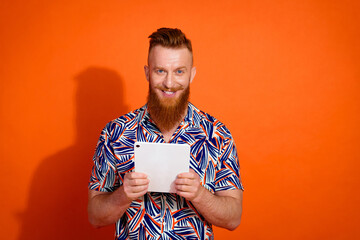Portrait of cheerful intelligent man with red long beard wear print shirt hold tablet in arms isolated on vibrant orange color background