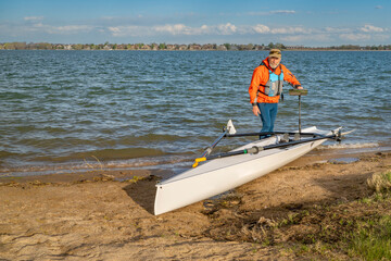 Senior male rower with his rowing shell on a beach of Boyd Lake in northern Colorado, serly spring...