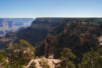 Explore breathtaking panoramic view of Grand Canyon under clear blue skies. Vast geological landscape showcases red and brown rock formations in Arizona, USA.