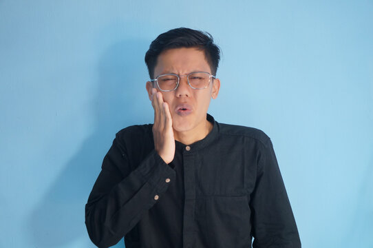 Asian young man in black shirt with toothache expression.