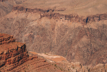 Rugged canyon landscape with layered rock formations in reddish brown hues showing erosion...